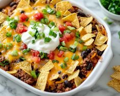 a white casserole dish filled with taco meat, cheese and tortilla chips