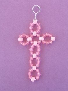 a pink beaded cross ornament on a purple background