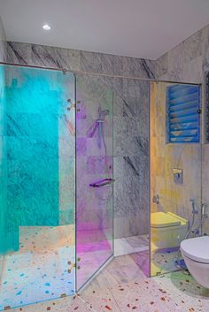 a bathroom with marble walls and flooring has a glass shower stall, toilet and sink