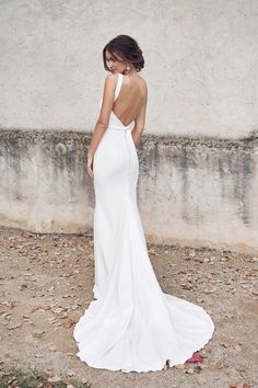 a woman in a white dress is standing near a wall and looking at her back