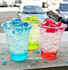 three different colored glasses sitting on top of a cement table next to eachother