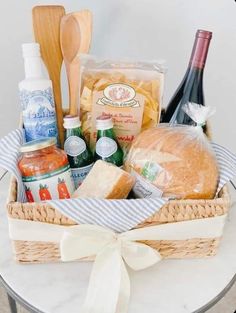 a basket filled with bread, cheeses and wine on top of a white table