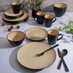 a table set with black and beige plates, cups, spoons and utensils