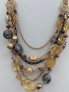 "Beautiful elegant multilayered necklace.  Lobster claw closure. Shortest layer is 23 \", longest 28\", extension 3\".  Six layers , 3 with beads and three without, only chains.  Beads include crystals, glass beads, foiled beads, acrylic beads.  Chains are one black and two gold tone. Connectors have clear rhinestones.  Weight 3.5 oz." Layered Multi-strand Metal Jewelry, Multi-strand Gold Beads Costume Jewelry, Multi-strand Layered Necklace For Parties, Layered Multi-strand Chain Necklace For Party, Layered Multi-strand Necklace For Parties, Gold Multi-strand Necklace With Gold Beads, Gold Layered Necklace With Round Beads, Elegant Yellow Multi-strand Necklace, Gold Double Strand Jewelry With Dangling Beads