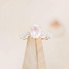 a pink diamond ring sitting on top of a wooden stand