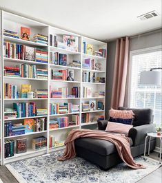 a living room filled with lots of books on top of a white book shelf next to a window