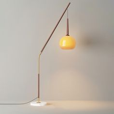 a yellow floor lamp sitting on top of a white table next to a gray wall