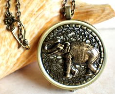 "Music box pendant. This round music box pendant is inspired by the gorgeous music box pendants of era's gone by. Music box is pill box size, please look at the dimensions for exact size. A round locket has been adorned with a layer of bronze filigree and a walking elephant. The filigree and elephant have been covered in a clear resin to give a glass like finish and preserve the beauty of this musical pendant. The locket opens and closes by pushing the little button on the side and reveals a tin Antique Finish Brass Round Pendant Locket Necklace, Bronze Round Brass Locket Necklace, Antique Bronze Locket Necklace With Round Pendant, Antique Bronze Round Pendant Locket Necklace, Antique Bronze Round Locket Necklace, Bronze Medallion Locket Necklace Gift, Bronze Medallion Locket Necklace For Gift, Handmade Round Brass Locket Necklace, Antique Finish Locket Necklace As Gift