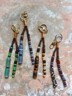 four beaded key chains are sitting on a stone surface and one is hanging from a metal hook