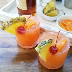 two glasses filled with drinks sitting on top of a wooden table next to bowls of fruit