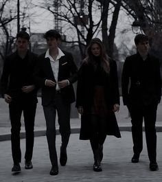 four people walking down the street in front of some trees and one person is wearing a black coat