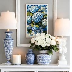 blue and white vases are sitting on a table next to a painting with flowers in it