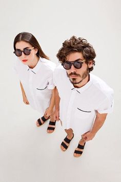 a man and woman in white shirts with sunglasses on their faces, standing next to each other