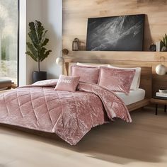 a bed with pink comforter and pillows in a room next to a window,