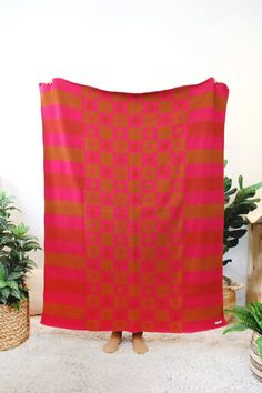 an orange and pink blanket sitting on top of a white floor next to potted plants