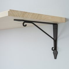 a wooden shelf with metal brackets on it and a white wall in the back ground