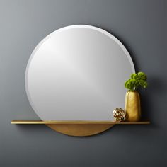 a round mirror sitting on top of a shelf next to a vase with a plant in it