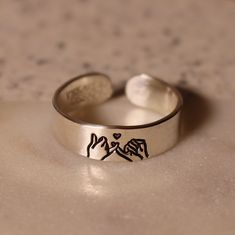 Looking for the perfect promise ring for your best friend or partner? This design features a pinky swear with two human hands, and a tiny heart above, representing the promise the ring creates. Product Details: Materials: Sterling Silver, Fine Silver, or Gold Filled Color: Silver or Gold Size: 6mm You will receive one hand-stamped ring filled with a black enamel finish. Adjustable Heart Ring For Promise And Mother's Day, Adjustable Heart Ring For Promise On Mother's Day, Personalized Sterling Silver Rings For Friendship, Adjustable Heart Toe Ring For Promise, Adjustable Minimalist Heart Ring For Promise, Adjustable Personalized Rings For Friendship, Personalized Adjustable Rings For Friendship, Symbolic Adjustable Heart Ring As Gift, Minimalist Personalized Promise Heart Ring