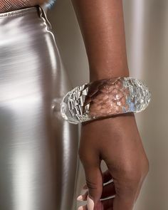 Close-up of a person’s hand wearing a large, clear, hand-sculpted Croc Lucite Cuff Bracelet by Nik Spruill, with a metallic skirt visible in the background. Lucite Bangle Bracelets As Gift, Lucite Bangle Bracelet As Gift, Lucite Bangle Bracelet For Gift, Modern Party Cuff Bangle Bracelet, Clear Bracelet Jewelry For Party, Elegant Plastic Jewelry For Parties, Luxury Glass Jewelry For Party, Elegant Clear Bracelets As Gift, Elegant Clear Bracelet As Gift