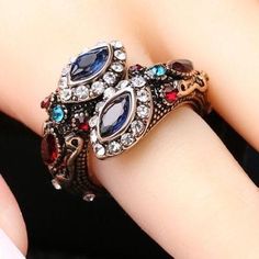 a woman's hand wearing a ring with blue, red and white stones on it