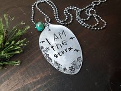 i am the storm necklace with green bead on it next to evergreen branches and pine cones