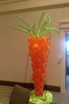 a balloon sculpture made to look like a carrot with green stems and oranges on it