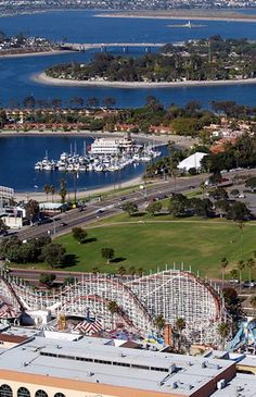 an aerial view of a carnival park and the ocean with boats in the water behind it