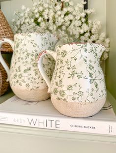 two white pitchers sitting on top of a book