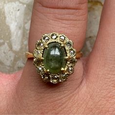 a close up of a person's hand wearing a ring with a green stone