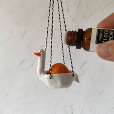 someone is holding an orange in the shape of a bird hanging from a bottle on a chain