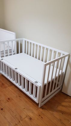 a white crib sitting on top of a hard wood floor