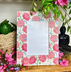 a pink flowered photo frame sitting on top of a wooden table next to a potted plant