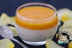 an orange and white dessert in a small glass bowl on a blue table cloth with flowers around it