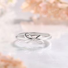 a silver ring with a bow on the side and flowers in the backgroun