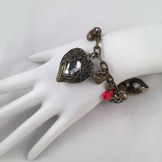 a white mannequin holding a bracelet with charms on it's sides and a red bead at the end