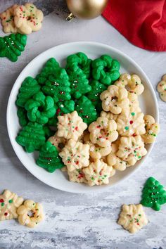 a plate full of cookies with green and red sprinkles on them next to christmas trees