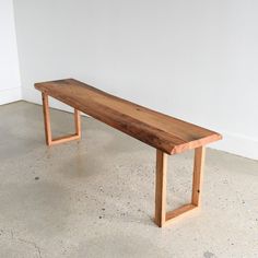 a wooden bench sitting on top of a cement floor next to a white wall in an empty room