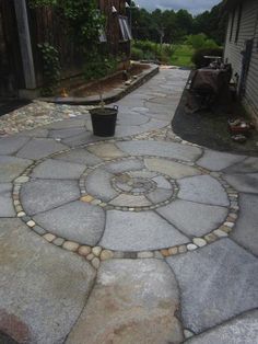 a stone walkway with a potted plant in the center and an old house in the background