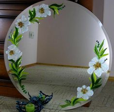 a mirror with flowers painted on it in the middle of a room next to a dresser