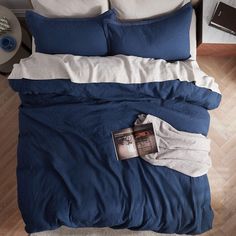 a blue comforter with white pillows and a magazine on the pillowcase next to it