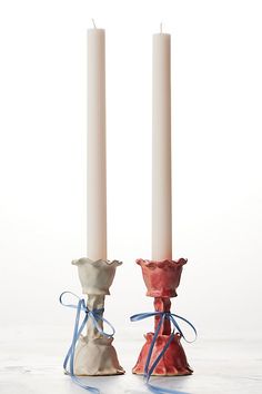 two white candles with blue ribbons tied around them on top of each other in front of a white background