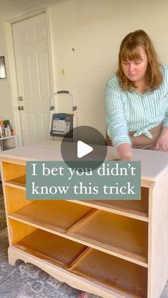 a woman sitting on top of a wooden table next to a book shelf with drawers