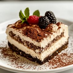 a piece of cake on a white plate with chocolate sprinkles and raspberries