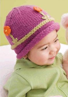 a baby is holding a teddy bear wearing a knitted hat with flowers on it