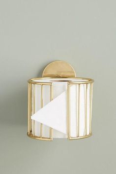 a white napkin holder with a gold finish on a gray wall next to a paper towel dispenser