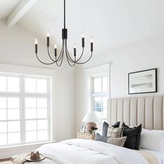 a bedroom with a large bed, chandelier and windows in the room that have white walls