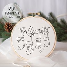 a christmas stocking and stockings embroidery pattern on a white background with pine cones, evergreen needles and an ornament hanging from the hoop