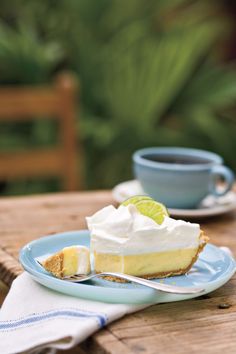 a slice of lemon pie on a plate with a fork and cup in the background