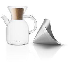 a white coffee pot next to a silver cone shaped object on a white surface with a wooden top