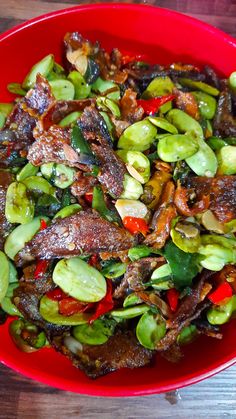 a red bowl filled with meat and veggies on top of a wooden table